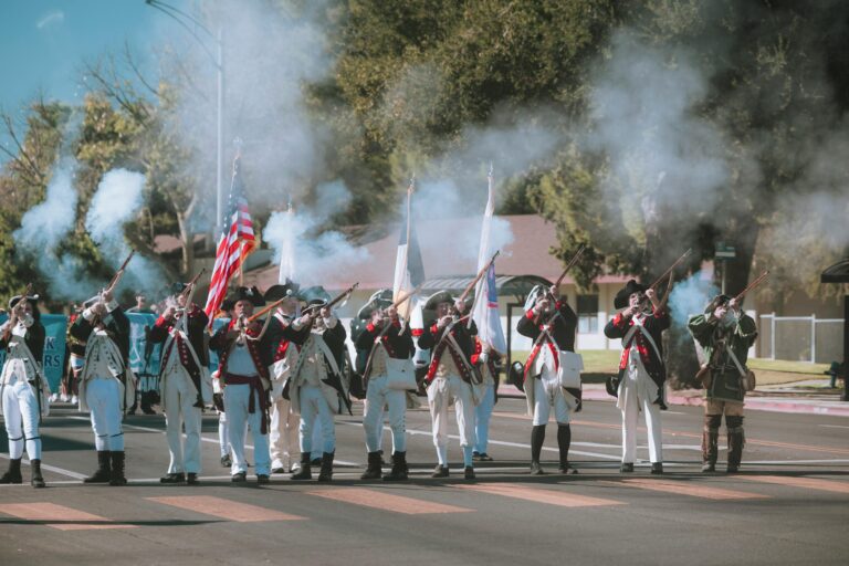 Participants in period costumes fire muskets in a dynamic historical reenactment parade.