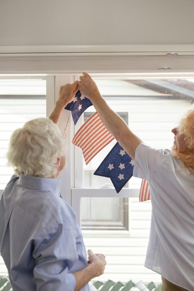 Elderly couple hanging American flag-themed decorations for a patriotic celebration indoors.